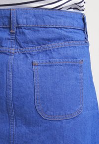 Modrá džínová sukně s viditelnou zadní kapsou a oranžovým prošitím, nošená s bílým a námořnickým pruhovaným topem.