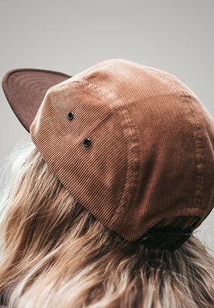 Braune Cord-Umhütze mit einem dunkelbraunen Schirm, ausgestattet mit zwei schwarzen Belüftungsöffnungen und einem schwarzen verstellbaren Riemen auf der Rückseite.