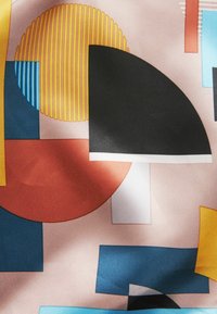 Tela estampada que presenta formas geométricas en negro, naranja, amarillo, azul y blanco sobre un fondo rosa claro; textura suave.