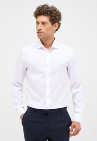 Witte lange mouwen overhemd met een klassieke kraag en knopenfront met gouden hardware. Soepele stof met een slim fit ontwerp. Donkere broek zichtbaar.