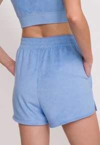 Ljust blå lounge-shorts gjorda av mjukt tyg, med ett elastiskt midjeband, sidofickor och en lätt rundad nederkant.