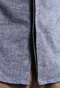 Tejido de lino azul con un acabado texturizado, que presenta un pequeño detalle bordado en blanco en el dobladillo y un diseño dividido para facilitar el movimiento.