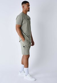 T-shirt in cotone verde chiaro con maniche corte e scollo rotondo, abbinato a pantaloni cargo verde chiaro con tasche laterali e dettagli neri.