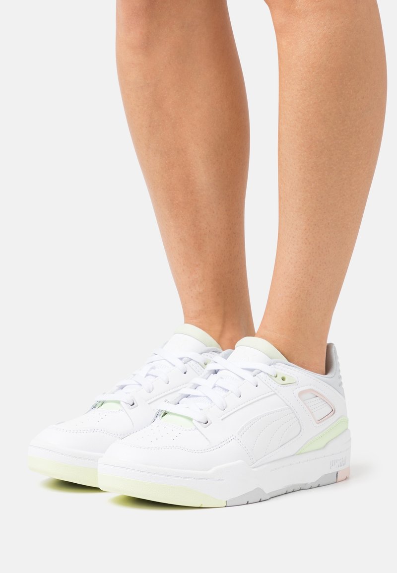 Chaussures de sport blanches avec une tige en cuir lisse, des accents vert clair, une languette rembourrée et une semelle en caoutchouc texturée présentant un design minimaliste.