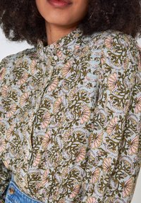 Långärmad skjorta med knappfunktion som har ett blommönster i rosa och grönt på en ljusblå bakgrund, tillverkad av lättviktsmaterial.