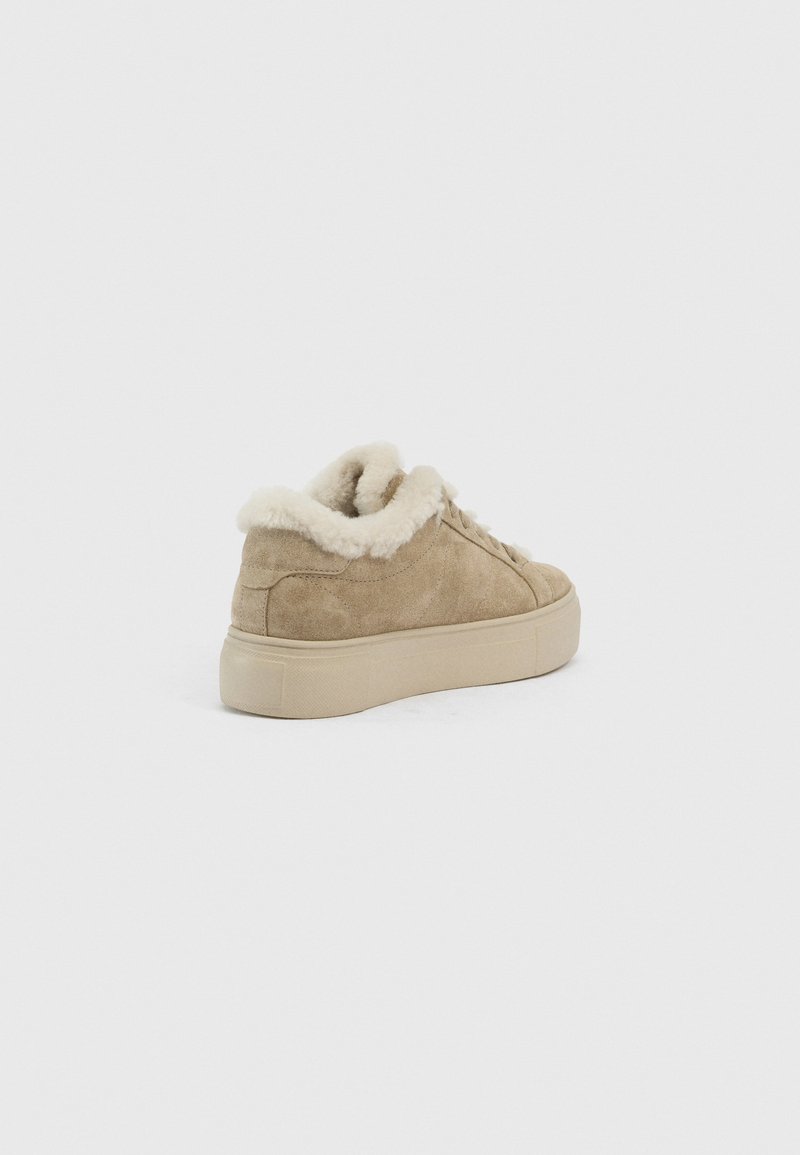 Beige Wildledersneaker mit dicker Gummisohle, rund um den Knöchel mit weißem plüschigem Fell gefüttert, von einer Rückansicht gezeigt.
