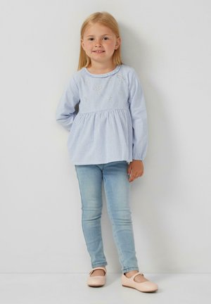 Top a maniche lunghe a righe blu e bianche con vita arricciata, abbinato a jeans fitted blu chiaro e scarpe flat rosa pallido.