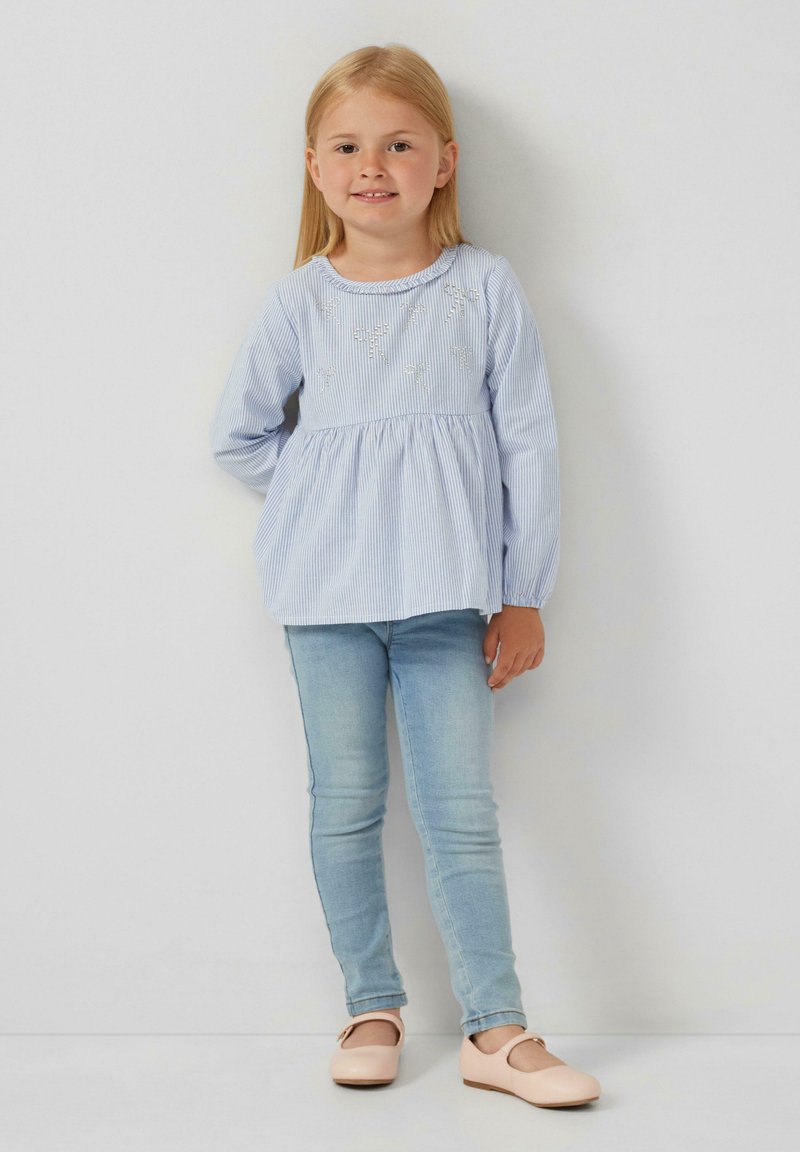 Top a maniche lunghe a righe blu e bianche con vita arricciata, abbinato a jeans fitted blu chiaro e scarpe flat rosa pallido.
