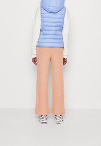 Jasnoniebieska kamizelka puchowa z kapturem, biała bluzka z długim rękawem oraz brzoskwiniowe szerokie spodnie. Srebrne sneakersy z czerwonymi i niebieskimi akcentami.