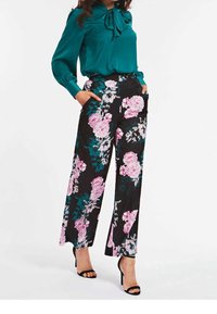 Blommiga vida byxor i svart tyg, med mönster av rosa och teal blommor. Kombineras med en teal-blus och svarta öppna klackskor.