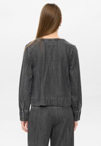 Giubbotto in denim grigio con maniche lunghe, polsini elasticizzati e scollo arrotondato. Presenta una vestibilità comoda e dettagli di cucitura visibili.