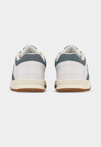 Ζευγάρι αθλητικά παπούτσια χαμηλού τύπου με λευκό δέρμα και σκούρες γκρι υφασμάτινες λεπτομέρειες, απεικονισμένα από πίσω σε απλό φωτεινό φόντο.