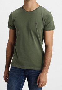 Olivgrünes Baumwoll-T-Shirt mit rundem Halsausschnitt, kurzen Ärmeln und einem kleinen gestickten Logo auf der Brust. Figurbetonter Schnitt.