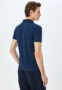 Marinblå polo t-shirt i blandning av bomull, med korta ärmar, ribbad krage och subtil textur på manschetternas accenter.