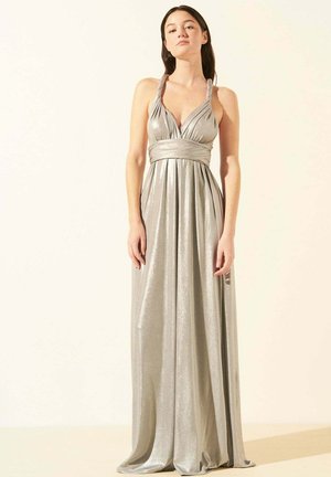 Robe argentée, longueur au sol, faite d'un tissu brillant. Présente un décolleté en V profond et des bretelles torsadées, avec une taille cintrée et une jupe fluide.