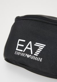 Pochette de voyage noire avec une fermeture éclair, arborant le logo blanc "EA7 EMPORIO ARMANI" bien en évidence sur le devant.