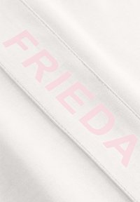 Witte stof met een gladde textuur met het woord "FRIEDA" in grote, lichtroze letters langs een naad.