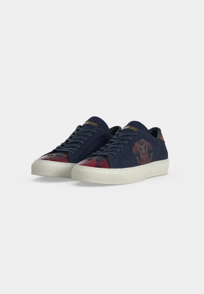 Ναυτικές sneakers χαμηλού προφίλ με λευκές σόλες, κόκκινο σχέδιο φιδιού στο μπροστινό μέρος και λογότυπο στο πλάι, χρυσό όνομα μάρκας στη γλώσσα και στην ταμπέλα της φτέρνας.