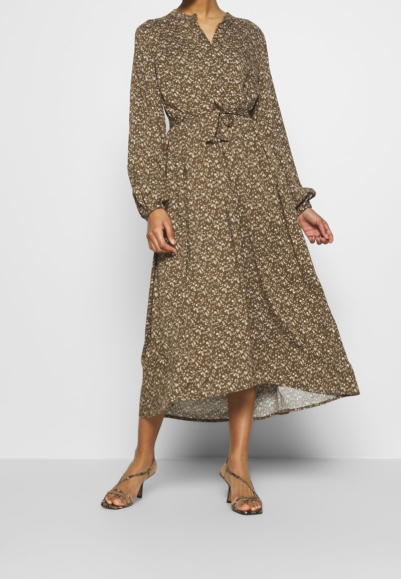 Abito lungo a maniche corte marrone floreale con cintura annodata, collo alla camicia e design fluido, caratterizzato da un orlo leggermente asimmetrico.