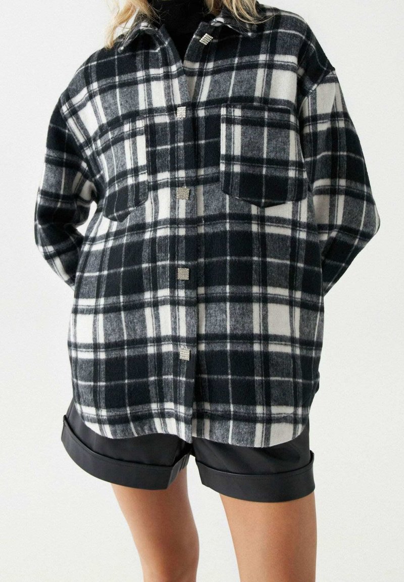 Randig skjorta i svart och vitt med en avslappnad passform, två framfickor och silverfärgad knappdetalj. Tillverkad av mjukt, strukturerat tyg.