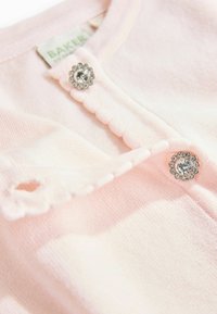Ljusrosa kofta med rund hals, med vågiga kanter och två knäppningar med rhinestones. Mjuk stickad textur.