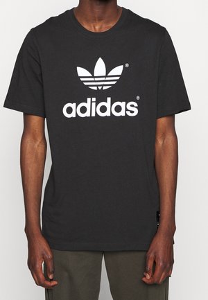 Camiseta de algodón negra con un gran logo blanco de trébol de Adidas. Diseño de manga corta y cuello redondo. Textura suave.