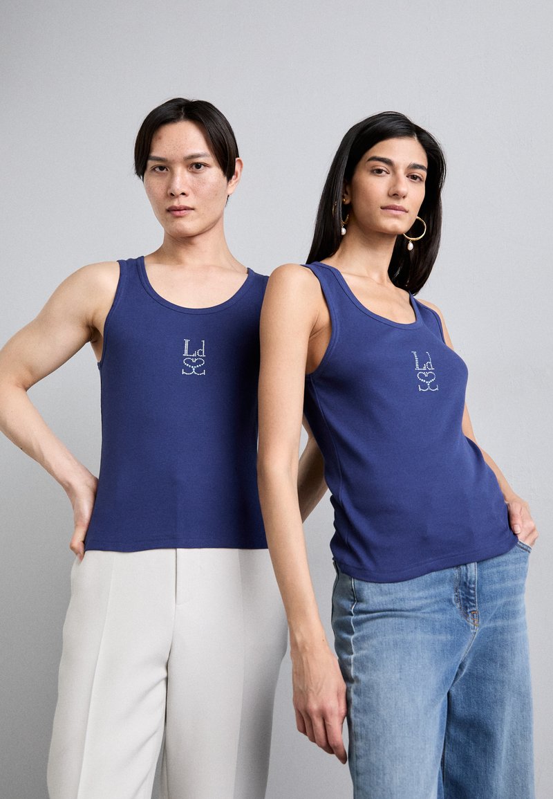 Zwei Personen tragen ärmellose Oberteile in Marineblau aus weichem Stoff, die auf der Vorderseite ein dezentes, bedrucktes Logo zeigen.