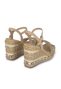 Sandales compensées beiges avec des textures tressées, ornées de strass clairs et de matériaux d'accent, dotées de brides de cheville réglables.