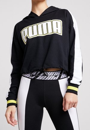 Czarna krótka bluza z kapturem z białymi rękawami i żółtymi mankietami, duże logo "PUMA", zestawiona z czarno-białymi legginsami z paskiem Puma.