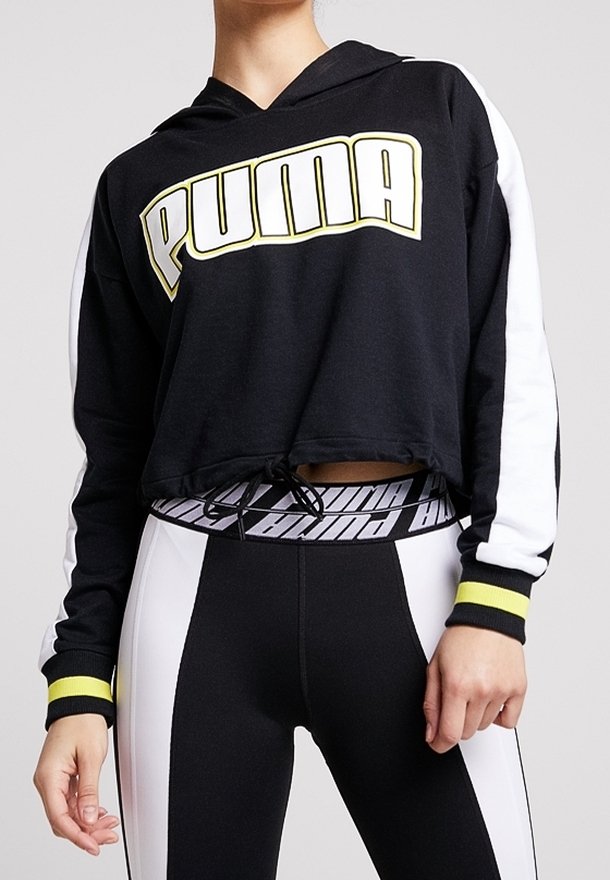 Sweat à capuche court noir avec manches blanches et poignets jaunes, grand logo "PUMA", associé à des leggings noirs et blancs avec ceinture Puma.