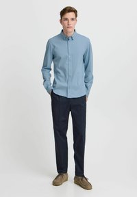Light blue button-up shirt with long sleeves, paired with dark navy trousers and gray moccasin shoes, set against a plain background.