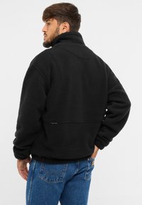 Pullover in pile nero con colletto alto, texture morbida, cuciture delle spalle a caduta e un accento sottile sull'orlo, abbinato a jeans blu.