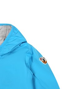 Giacca impermeabile azzurro chiaro con cappuccio, dotata di una fodera interna grigia e una patch colorata sulla manica sinistra. Texture liscia e opaca.