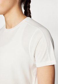 Camisa atlética blanca de manga corta. Cuenta con una tela suave, un cuello redondo y paneles de malla a lo largo de los lados para mayor transpirabilidad.