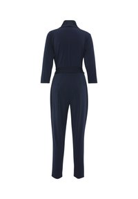 Tuta blu navy con maniche lunghe, colletto e vita aderente. Presenta gambe affusolate e un tessuto liscio e elastico. Vista posteriore mostrata.