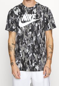 Grå kamouflage kortärmad t-shirt med en stor vit Nike-logotyp på framsidan, gjord av en lätt bomullsblandning.