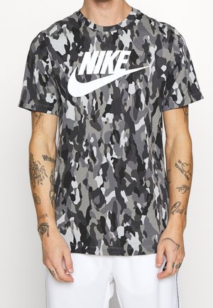 Graues Tarnmuster-T-Shirt mit kurzen Ärmeln, das auf der Vorderseite ein großes weißes Nike-Logo aufweist, aus einem leichten Baumwollmix hergestellt.
