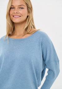 Jasnoniebieski sweter dziany z szerokim dekoltem, prążkowanymi mankietami i luźnym krojem. Miękka struktura, długie rękawy i minimalne detale.