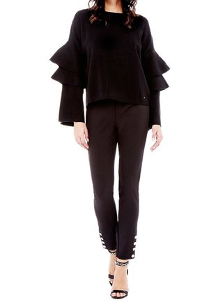 Pull noir avec des manches en volants superposés, associé à un pantalon noir avec des accents de boutons à l'ourlet. Complété par des talons noirs à brides.