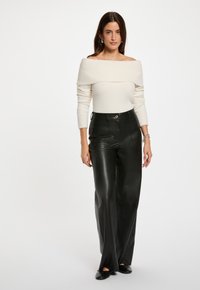 Maglione avorio scollato sulle spalle abbinato a pantaloni a gamba larga in pelle nera a vita alta. Accento di hardware argento semplice sui pantaloni. Texture morbide.