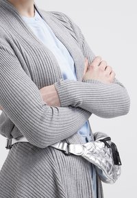 Cardigan grigio a coste con maniche lunghe e una cintura argentata trapuntata con cerniera, indossata in vita.