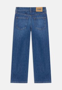 Jeans de mezclilla anchos azul con un parche de logo, dos bolsillos traseros y costura en contraste. Textura suave con un corte clásico.
