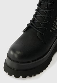 Fekete bokacsizma, textúrált bőrből, lekerekített orral, fűzős kivitelben, bordázott szintetikus talppal és szegecsel díszített oldallal.