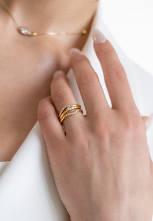Gouden ringstack met drie ringen: twee gedraaide gouden ringen en één met een marquise-steen omringd door kleine heldere stenen. Gladde textuur.
