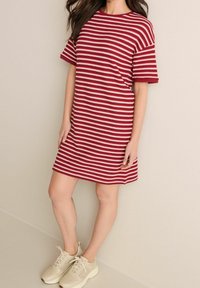 Rot-weiß gestreiftes Kleid mit kurzen Ärmeln und rundem Halsausschnitt, aus einem strukturierten Strickstoff. Kombiniert mit hellen Sneakers.