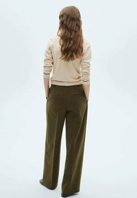 Pull beige avec des poignets côtelés associé à un pantalon large olive avec des poches latérales. Modèle vu de dos sur un fond clair.