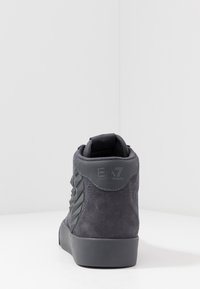 Grå högsnea med överdel i mocka, försedd med en texturerad sidopanel, märkesklack och en slät gummisula. Har en vadderad krage för extra komfort.