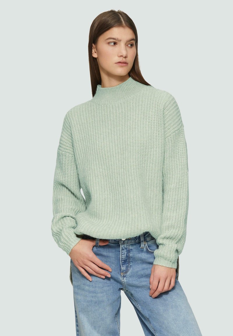 Lichtgroen gebreid sweater met een hoge hals, losse pasvorm en geribbelde textuur, gecombineerd met lichtblauwe jeans.