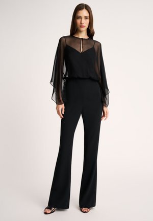Zwarte jumpsuit met doorschijnende, vloeiende mouwen en een diepe V-hals. Gladde stof met een getailleerde pasvorm, uitlopende broekspijpen en minimale hardware.