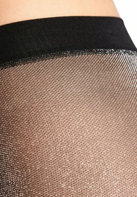 Czarne przezroczyste rajstopy z delikatnym wzorem z rombów typu siateczka, wyposażone w gładką elastyczną talię zapewniającą pewne dopasowanie i subtelny błysk.